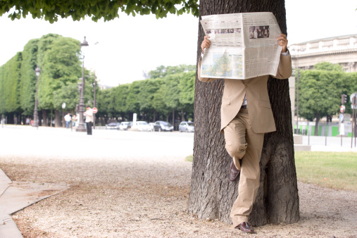 Spy hiding behin newsppaer in park